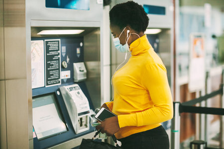 Dubai, UAE, November 2020 African woman wearing a protective mask withdraws money from a bank card at an ATMの写真素材