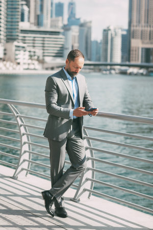 Young businessman with a phone in his hands, standing in a big city among high-rise buildings.の写真素材