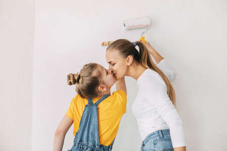 Beautiful and happy mom and daughter paint the walls in the apartment whiteの写真素材