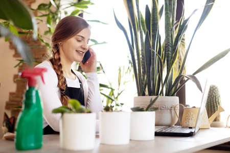 Portrait of a young female florist talking on the phone and using a laptop in a flower shop.の写真素材