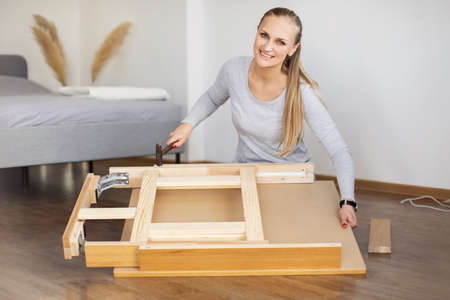 Happy woman collects furniture with a hammer in the bedroomの写真素材
