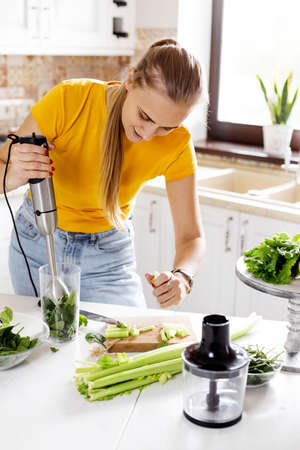 A young woman with a blender and green vegetables making a detox cocktail. Healthy food, cooking,...