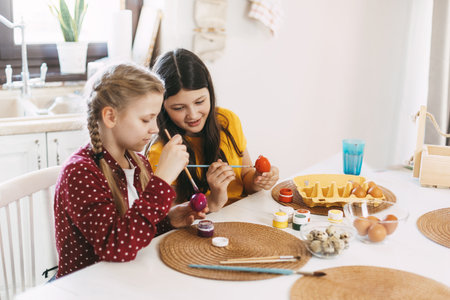 Two sisters are sitting at the table and painting Easter eggs in different colors for Easterの写真素材