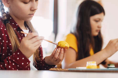 Two sisters are sitting at the table and painting Easter eggs in different colors for Easter, close-upの写真素材
