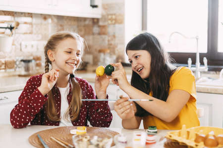 Two sisters are sitting at the table and painting Easter eggs in different colors for Easterの写真素材