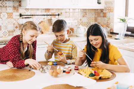 Funny and cheerful children sitting at the table paint Easter eggs in different colors for Easterの写真素材