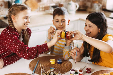 Funny and cheerful children sitting at the table paint Easter eggs in different colors for Easterの写真素材