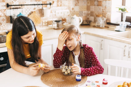 Two sisters are sitting at the table and painting Easter eggs in different colors for Easterの写真素材