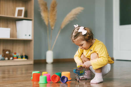 A beautiful little girl plays with toy molds and builds a pyramid on the floor of a house or kindergarten. Childhood, toys, happy timeの写真素材