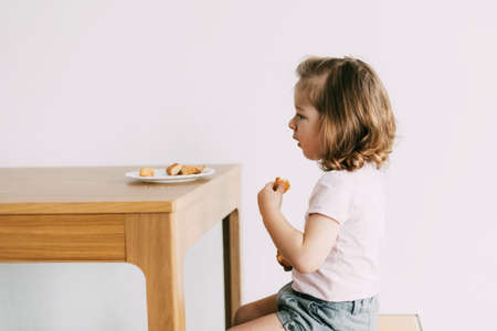 A little girl sits at a table and eats cookiesの写真素材