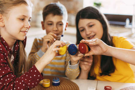 Funny and cheerful children sitting at the table paint Easter eggs in different colors for Easter