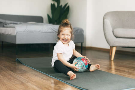 A small child plays on a sports mat with a ball
