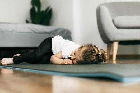 A little girl lies on a yoga mat in the bedroom and rests after a gameの写真素材