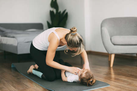 A young mother and her little daughter are getting ready to do fitness together in the bedroom of the houseの写真素材