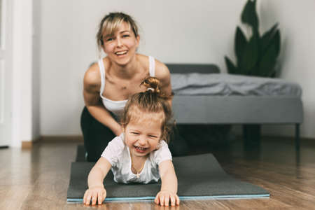 A young mother and her little daughter have fun on the mat before playing sportsの写真素材