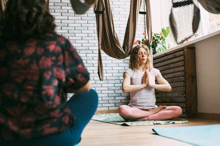 Two women sit on a mat in a yoga class and meditate after a workout. Rest, relaxation, meditationの写真素材