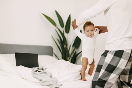 Dad is dancing on the bed with a child, smiling and having fun during a break at work on a laptopの写真素材