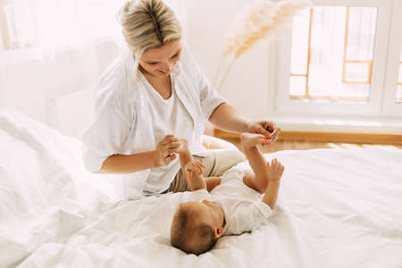 Happy mom plays with her little son lying on the bed, mom and baby relax together. Innocence, unity...