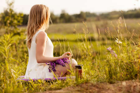 A young girl meditates in nature, a bouquet of lupines on her lap. Side view, space for textの写真素材