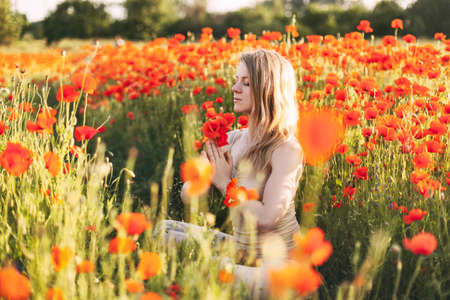 A beautiful girl with closed eyes meditates on a poppy field holding a bouquet of flowersの写真素材
