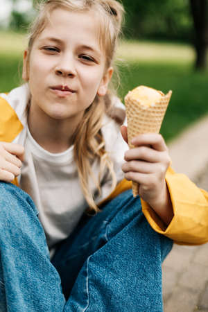 Portrait of a cute blonde teenage girl with ice cream on a walk in the park. Child outdoors