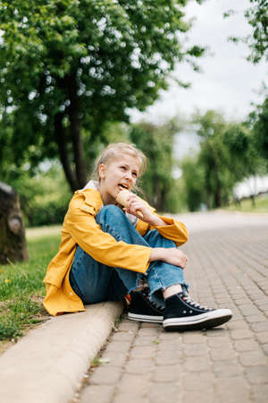 Portrait of a cute blonde teenage girl with ice cream on a walk in the park. Child outdoorsの写真素材