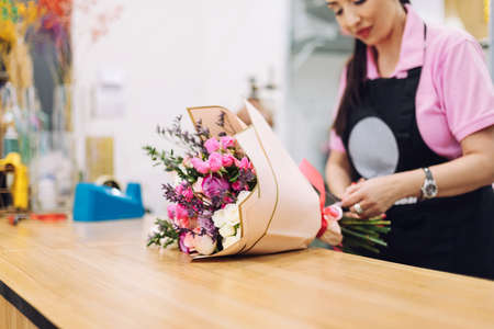 Close-up of a beautiful bouquet of flowers a florist girl is wrapping in gift paper. Flower business, working with flowers, flower bouquetの写真素材