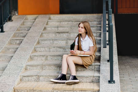 Cute girl sitting on the stairs outside the campus after college class and chatting with her friendsの写真素材