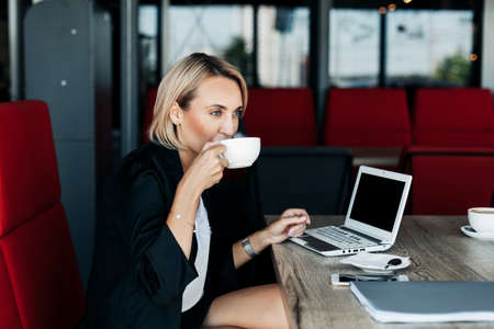 A young woman is drinking coffee in a cafe during a break and working at a laptop. Business conceptの写真素材