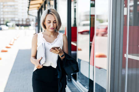 A stylish businesswoman is walking around the city, holding a folder with documents under her armの写真素材