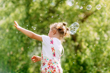 A cheerful girl catches soap bubbles with her hands. Happy childhood, summer time. Side viewの写真素材