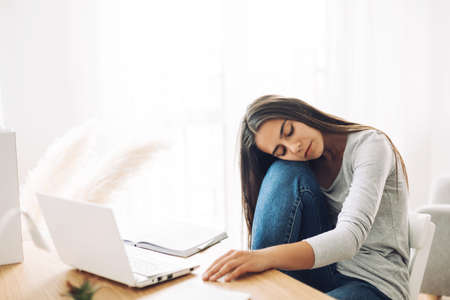 A student girl rests with her eyes closed, resting her head on her knees, while preparing for...