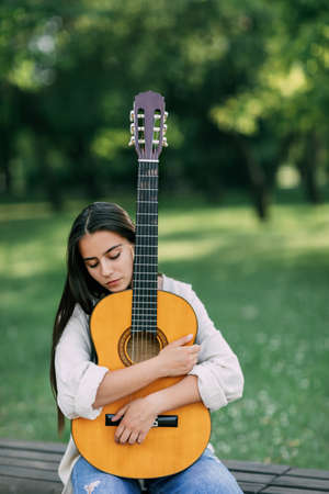 An attractive girl with a guitar in the park. The concept of creative hobbies and professionals. The girl is a musicianの写真素材