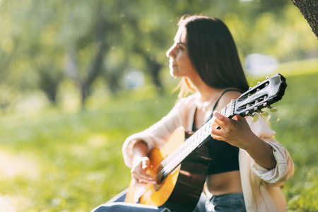 A girl in harmony with herself plays the guitar in the park. Hobbies, music, musicianの写真素材