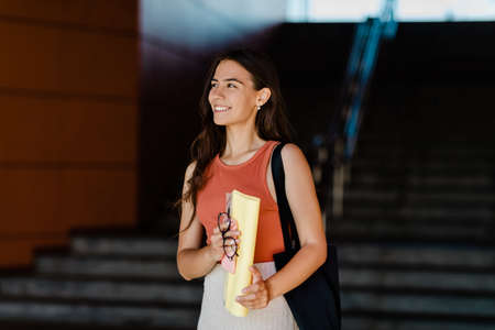 A smiling student girl stands on the steps and holds folders, glasses and a phone in her handsの写真素材