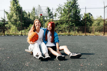 A couple of teenage girls on a sports street court with a basketball lifestyle relax after a game and talk. The concept of sports and a healthy lifestyleの写真素材