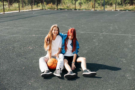 A couple of teenage girls on a sports street court with a basketball lifestyle relax after a game and talk. The concept of sports and a healthy lifestyleの写真素材