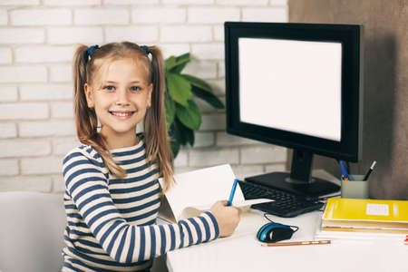 A blonde girl with beautiful ponytails is sitting at a computer at home, looking at the camera and...