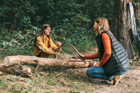 A mother and her daughter are sawing a fallen tree for a fire. Firewood harvesting, bonfire, picnicの写真素材
