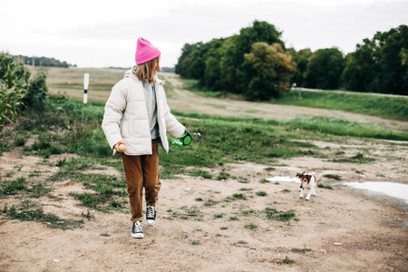 Cute teenage girl walking her dog Jack Russell Terrier on a leash in a field against a background of a cornfield in autumnの写真素材