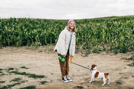 Cheerful teenage girl playing in the field with her dog Jack Russell Terrier on the background of a corn field in autumnの写真素材
