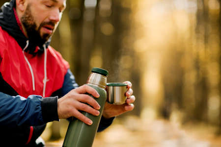 Close-ups of a man pouring tea into a cupwhile relaxing in an autumn park or forestの写真素材