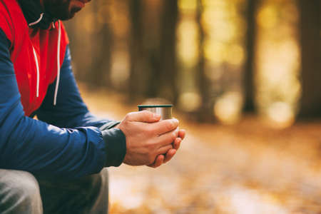 Close-up of a mans hands with a cup of hot drink in an autumn park or forestの写真素材