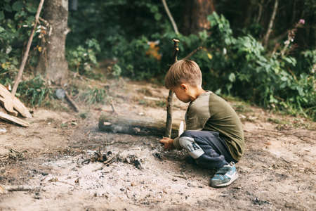 A boy-child makes a fire from wood branches in a forest camping. Camping in the forest in summer. Picnic in the fresh air. Family campの写真素材