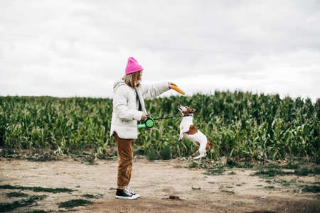 Cheerful teenage girl playing in the field with her dog Jack Russell Terrier on the background of a corn field in autumnの写真素材