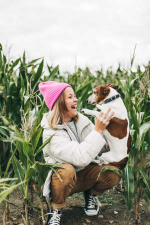 Happy teenage girl hugging her dog Jack Russell terrier in a field against a background of a cornfield in autumnの写真素材