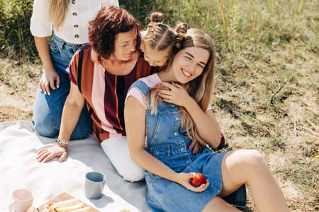 The family is having a picnic on the lawn. Three generations of women of the same family rest togetherの写真素材