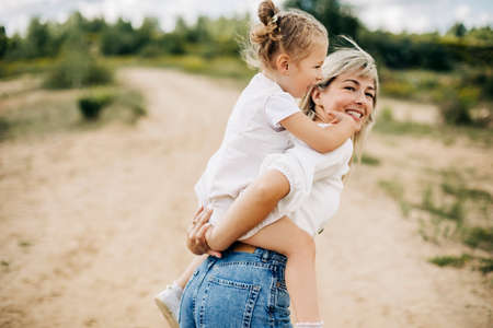A young mother rolls her little daughter on her back, the baby hugs her motherの写真素材