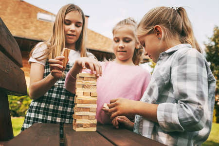 Three beautiful sisters are playing a wooden board game outdoors near their home.の写真素材