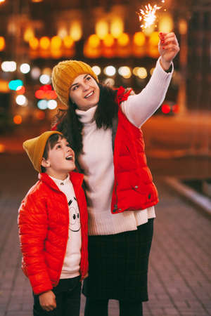 Portrait of a young woman and her son in bright clothes with sparklers. The concept of Christmas and...